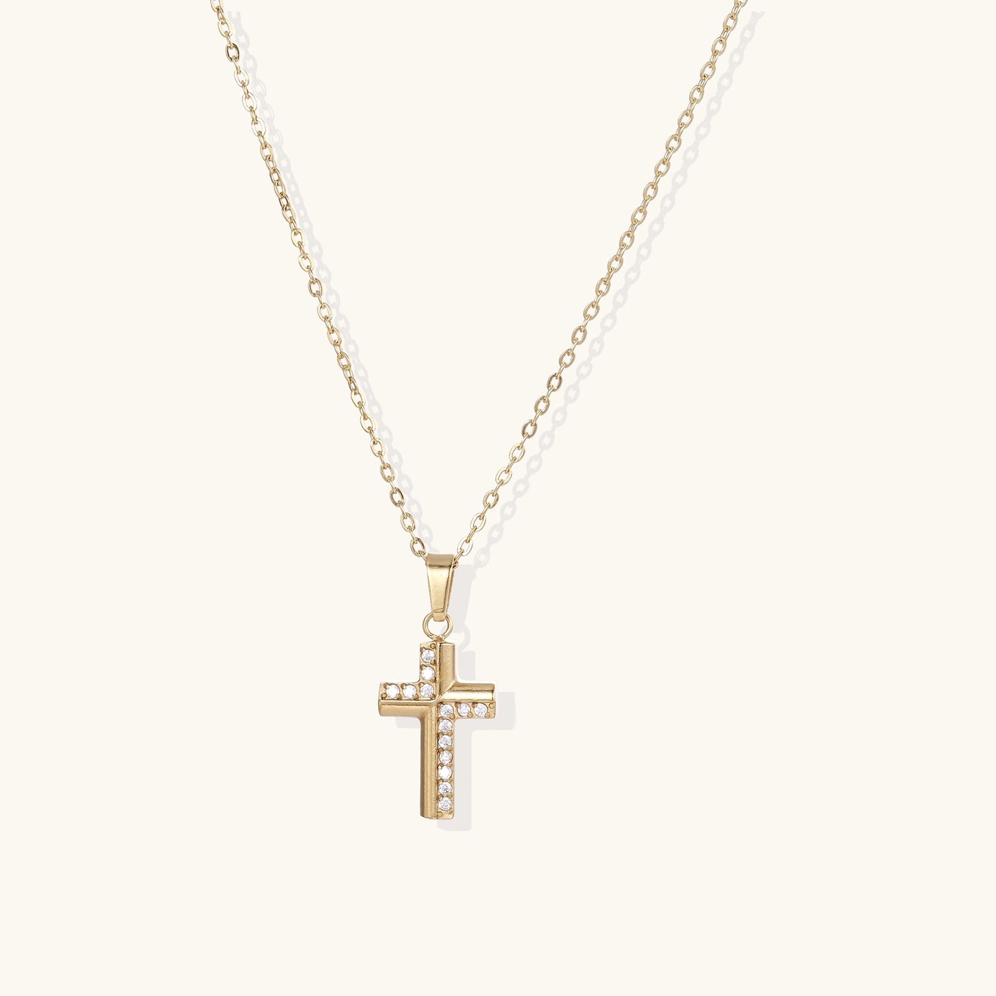Gold-plated cross pendant necklace with crystal accents on delicate chain against neutral background.